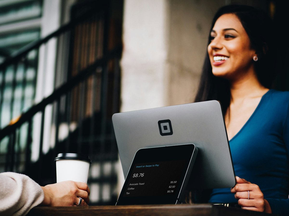 Smiling woman holding a laptop with a coffee cup on a desk in front of an urban building